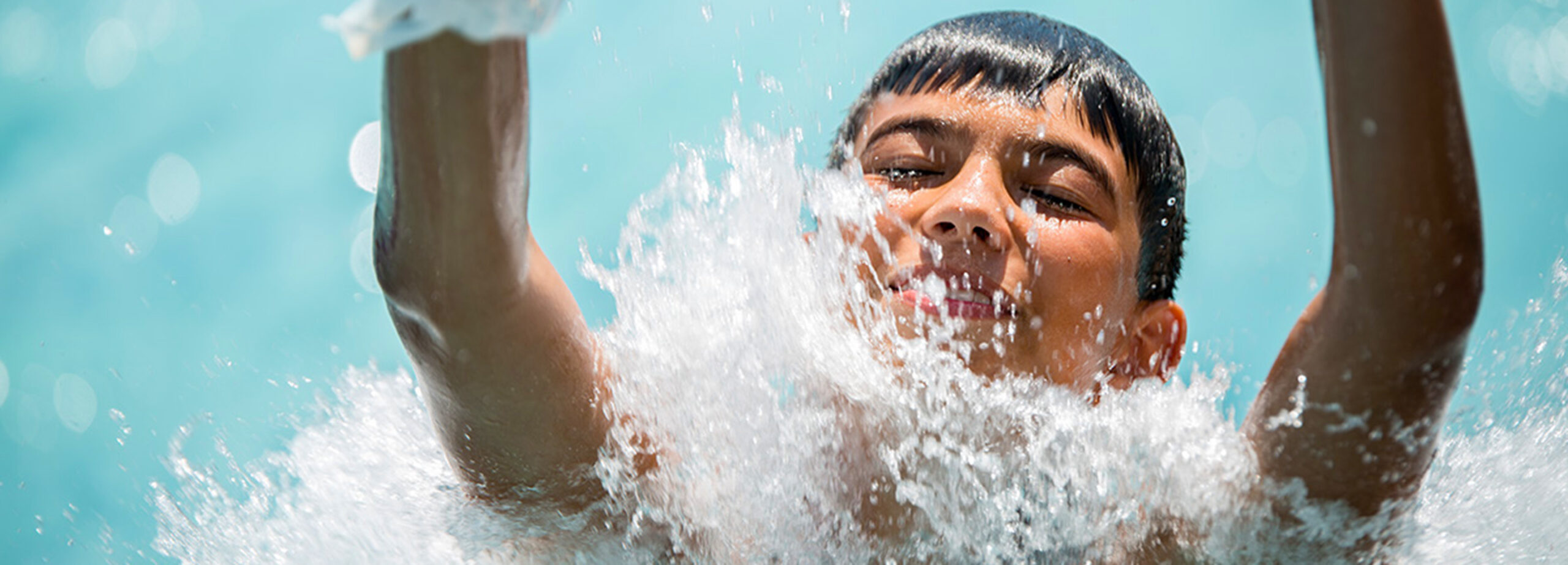 Blog Image A person splashes into the water at the bottom of a water slide, with water droplets in the air and their feet visible in the foreground.