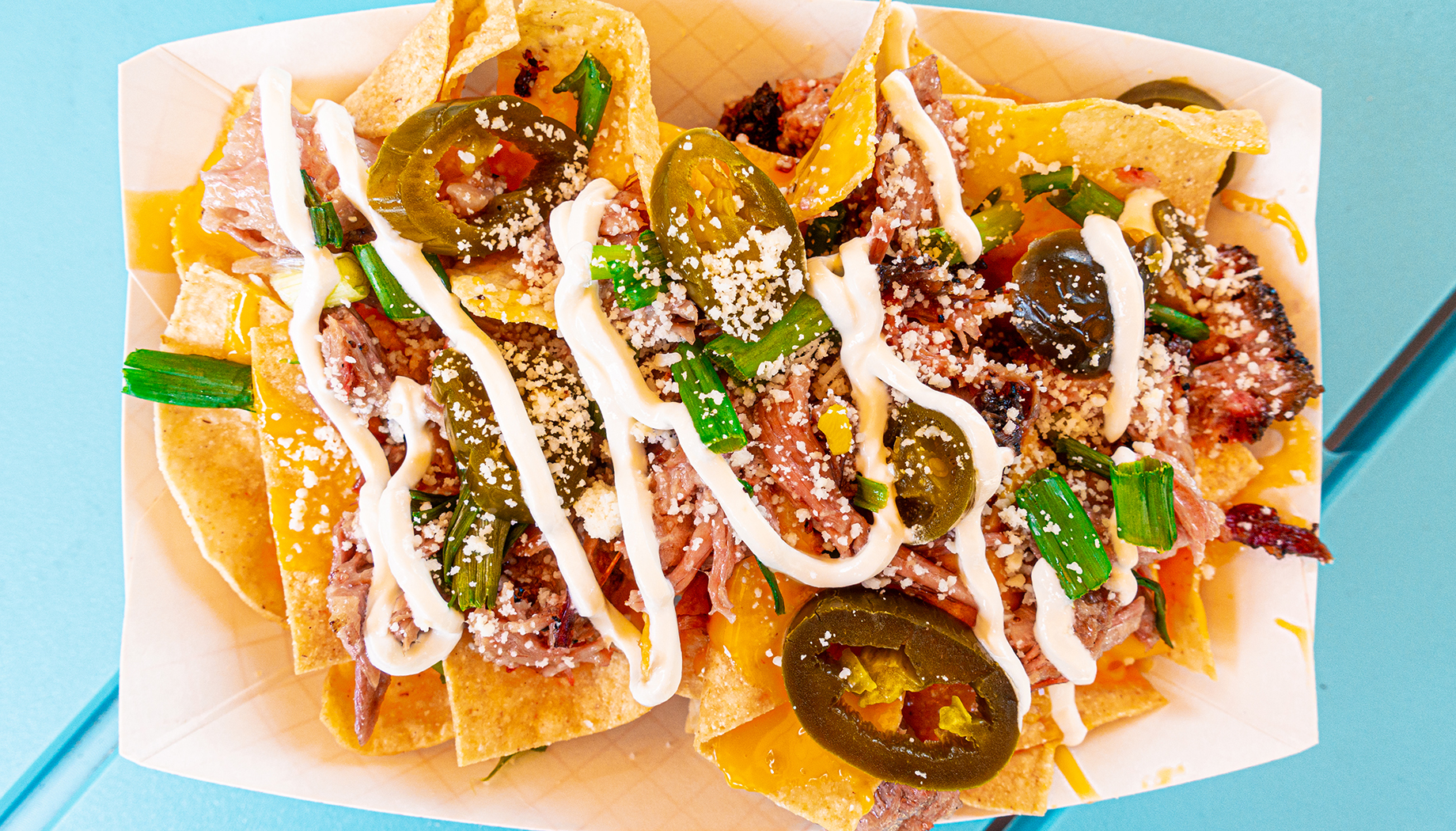 BLOG Nachos in a paper tray topped with barbecue meat, jalapeños, cheese, and more.
